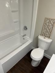 full bathroom with washtub / shower combination, toilet, and wood finished floors