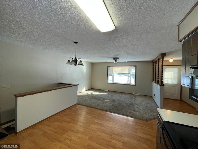 unfurnished living room with ceiling fan with notable chandelier, a textured ceiling, and light hardwood / wood-style floors