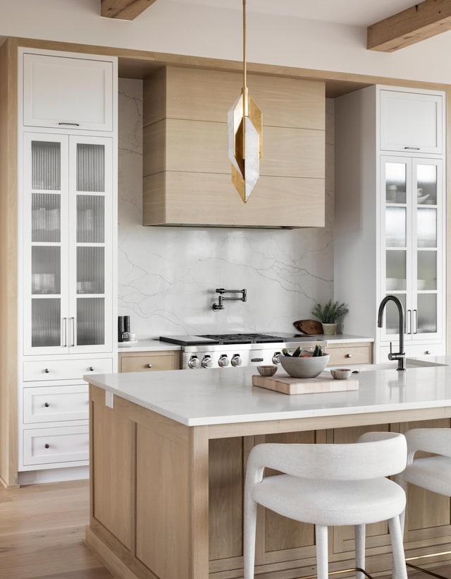 kitchen with white cabinets, light wood-type flooring, decorative light fixtures, and a kitchen island with sink