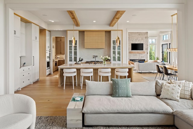 living room with beamed ceiling, light hardwood / wood-style floors, a fireplace, and sink