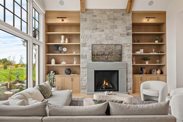 living room featuring hardwood / wood-style floors, built in shelves, a stone fireplace, and beamed ceiling