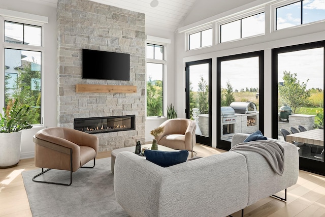 living room featuring light hardwood / wood-style floors, high vaulted ceiling, and a stone fireplace