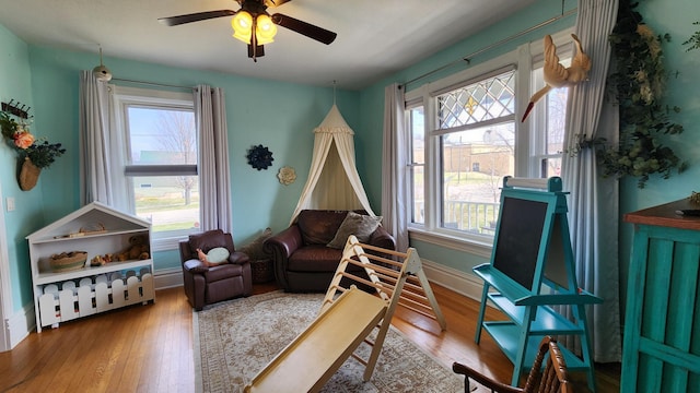 living area with baseboards, a ceiling fan, and wood finished floors