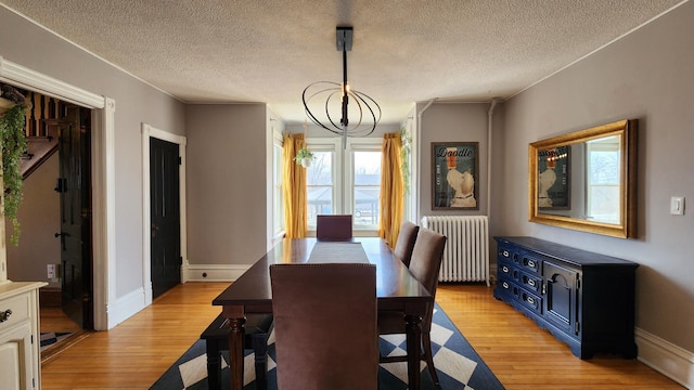 dining area with radiator, an inviting chandelier, light wood-type flooring, a textured ceiling, and baseboards