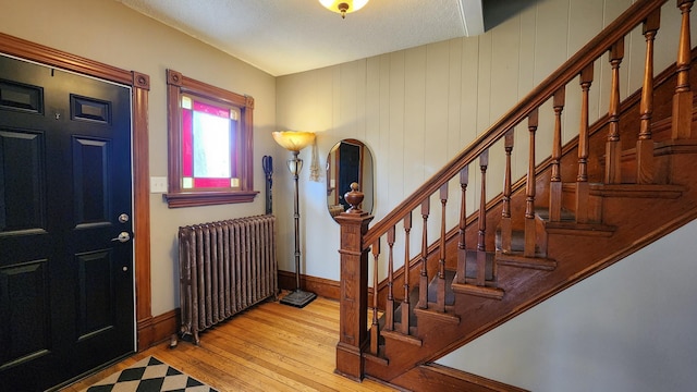 entrance foyer with a textured ceiling, radiator heating unit, stairs, baseboards, and hardwood / wood-style flooring