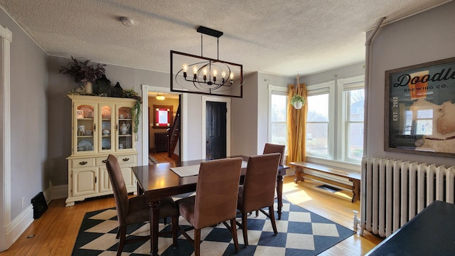 dining space with radiator heating unit, light wood finished floors, a notable chandelier, and a textured ceiling