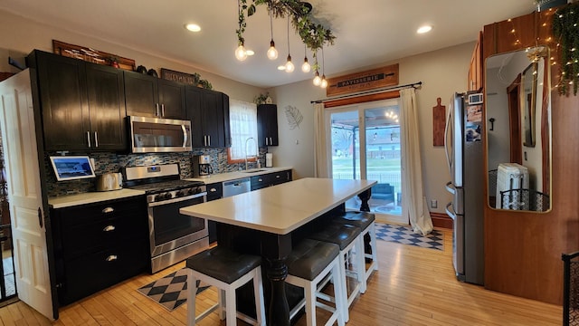 kitchen featuring dark cabinets, light wood-type flooring, a kitchen breakfast bar, light countertops, and stainless steel appliances