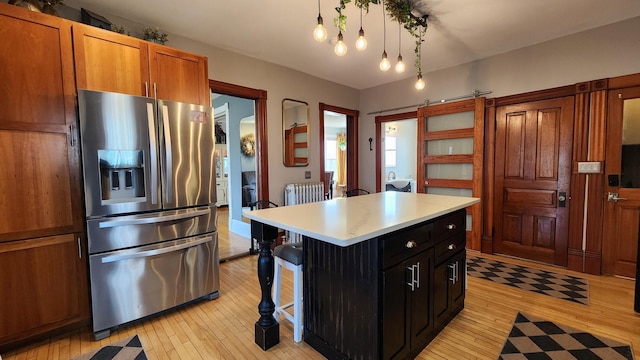 kitchen featuring light wood-type flooring, stainless steel fridge, light countertops, brown cabinets, and radiator