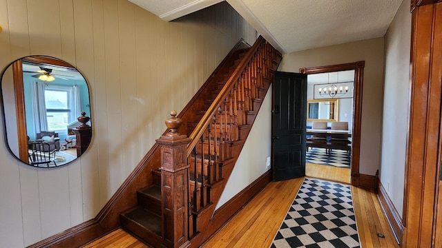 staircase with ceiling fan with notable chandelier, hardwood / wood-style floors, baseboards, and a textured ceiling