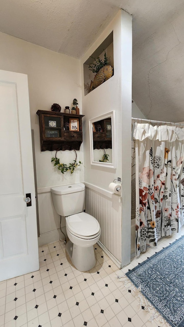 full bath with toilet, a textured ceiling, a shower with curtain, and baseboards