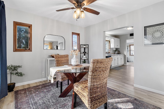 dining space featuring a ceiling fan, baseboards, and light wood finished floors