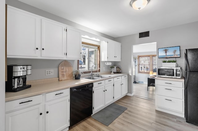 kitchen featuring light wood finished floors, visible vents, white cabinets, a sink, and black appliances