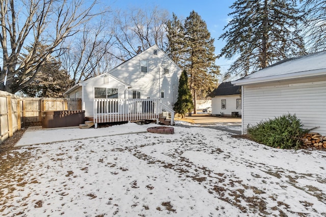 snow covered house featuring a chimney, fence, and a wooden deck