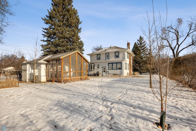 snow covered back of property with a sunroom