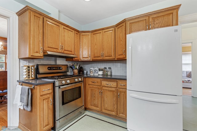 kitchen with stainless steel gas range oven, decorative backsplash, white fridge, and range hood