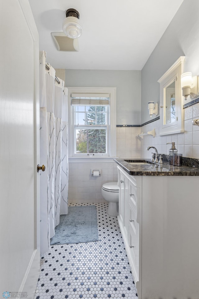 bathroom featuring toilet, vanity, tile patterned floors, and tile walls