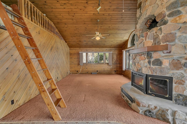 unfurnished living room featuring a ceiling fan, carpet floors, high vaulted ceiling, a stone fireplace, and wood walls