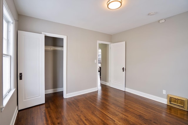 unfurnished bedroom with dark hardwood / wood-style flooring, a closet, and multiple windows