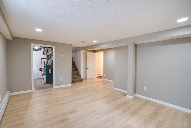 basement featuring light hardwood / wood-style floors, a textured ceiling, and a baseboard heating unit