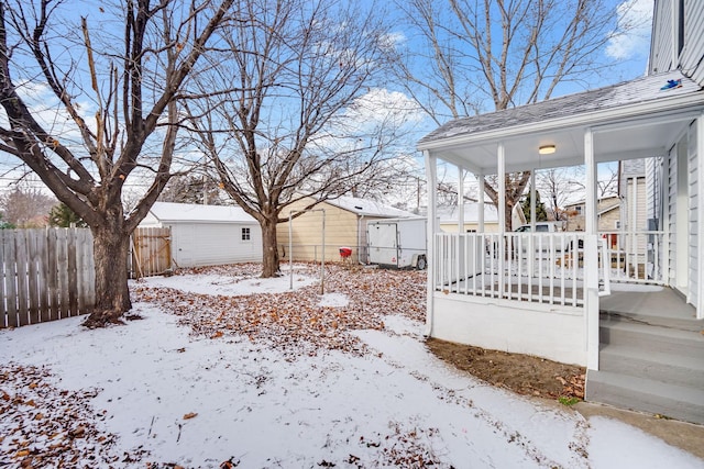 snowy yard featuring covered porch and an outdoor structure