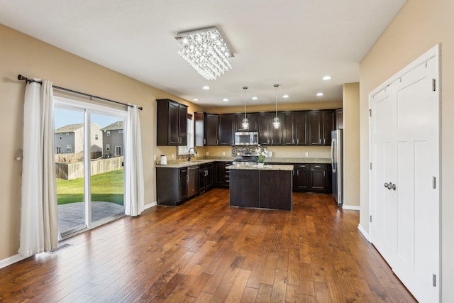 kitchen featuring dark hardwood / wood-style flooring, stainless steel appliances, sink, a center island, and hanging light fixtures