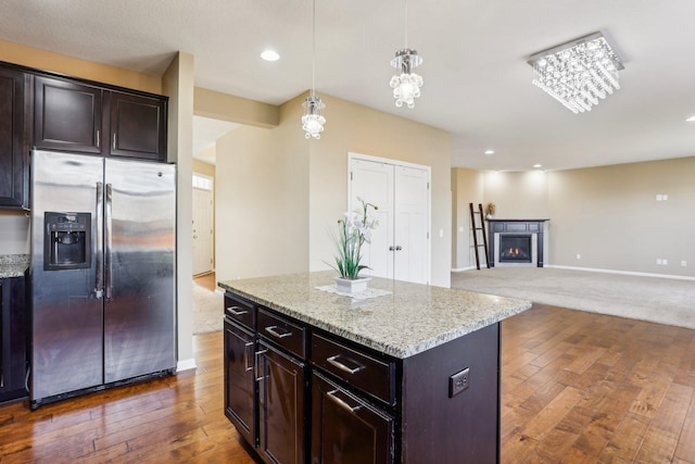 kitchen with light stone countertops, a center island, dark hardwood / wood-style flooring, stainless steel fridge, and decorative light fixtures