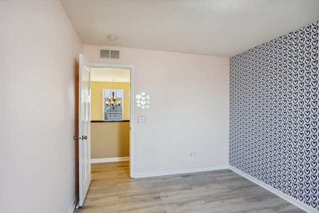 empty room featuring a textured ceiling, light wood-type flooring, and a notable chandelier