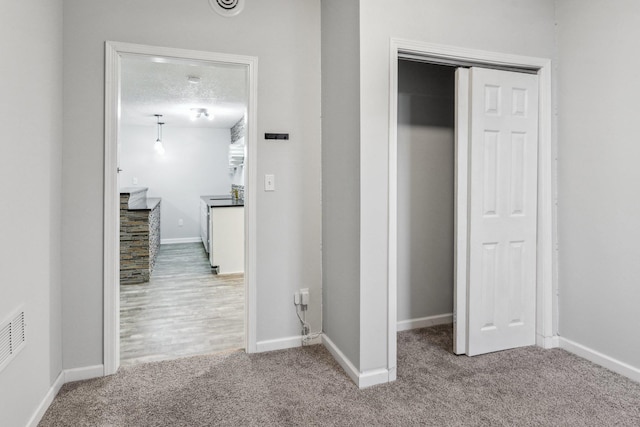 hallway with light colored carpet and a textured ceiling