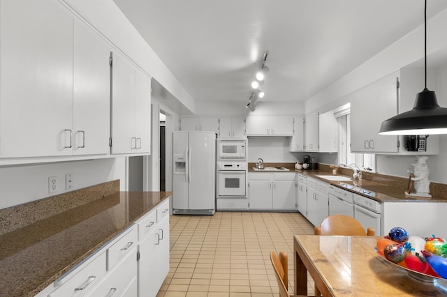 kitchen with a sink, white appliances, dark stone counters, white cabinetry, and light tile patterned floors