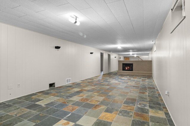 basement featuring visible vents, a brick fireplace, and stone tile flooring