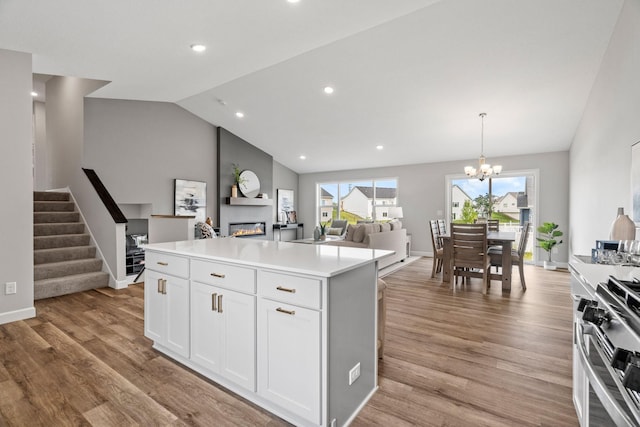 kitchen with a center island, stainless steel range with gas cooktop, vaulted ceiling, white cabinets, and light wood-type flooring