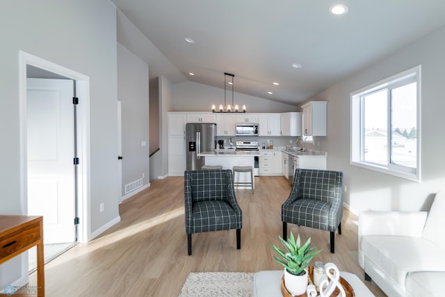 living room with light hardwood / wood-style floors, vaulted ceiling, a notable chandelier, and sink