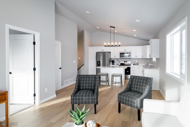 living room featuring a notable chandelier, light hardwood / wood-style floors, lofted ceiling, and sink