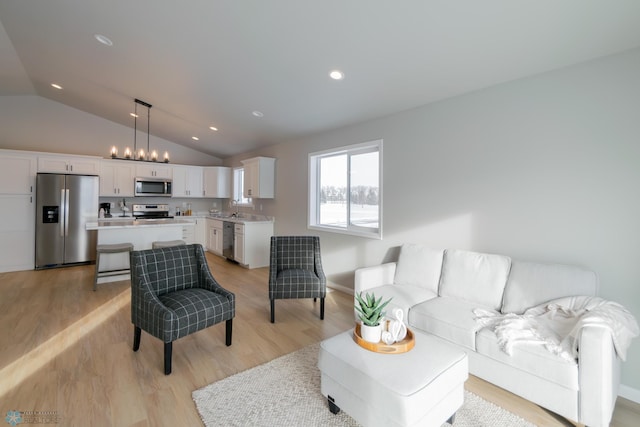 living room with sink, light hardwood / wood-style flooring, and vaulted ceiling