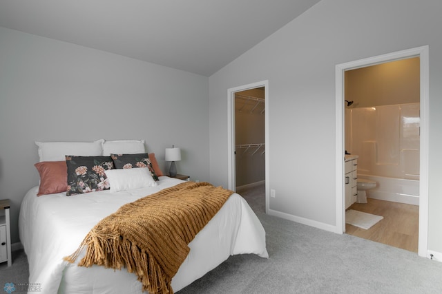 carpeted bedroom featuring a walk in closet, vaulted ceiling, a closet, and connected bathroom