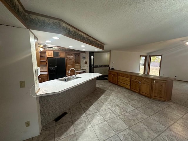 kitchen with sink, an island with sink, a textured ceiling, black refrigerator with ice dispenser, and light tile patterned floors