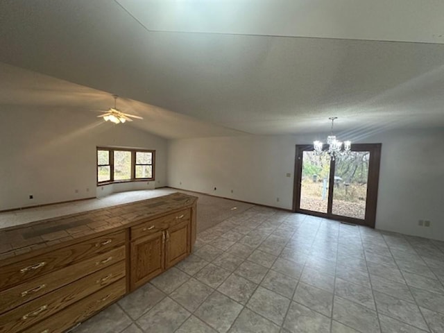 unfurnished living room with lofted ceiling, light tile patterned flooring, and ceiling fan with notable chandelier