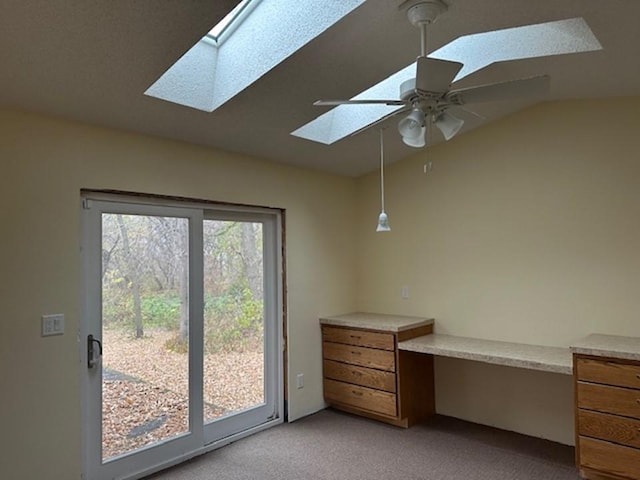 interior space with light carpet, lofted ceiling with skylight, built in desk, and ceiling fan