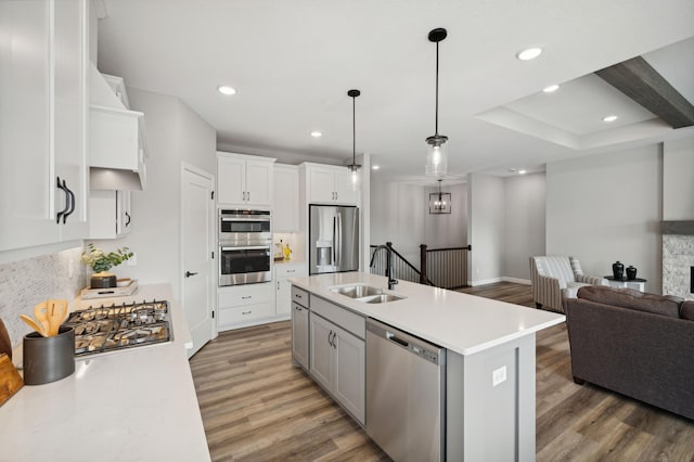 kitchen with appliances with stainless steel finishes, sink, hardwood / wood-style floors, white cabinets, and a center island with sink