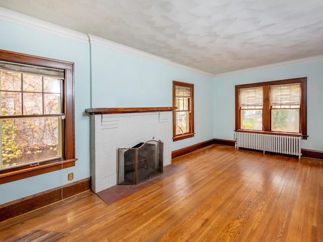 unfurnished living room with ornamental molding, radiator heating unit, wood-type flooring, and a brick fireplace