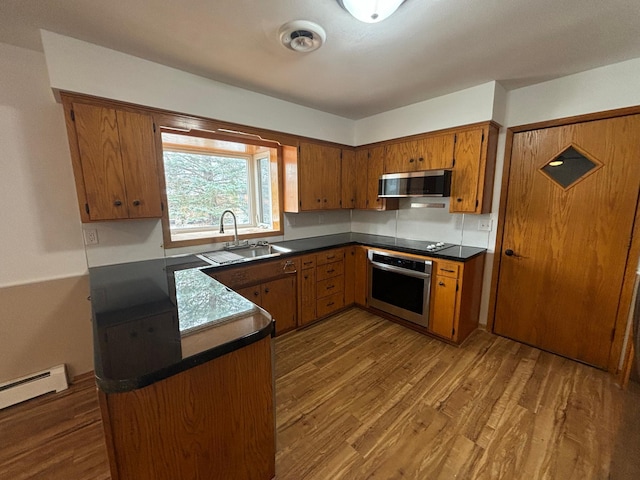 kitchen featuring appliances with stainless steel finishes, sink, kitchen peninsula, baseboard heating, and dark wood-type flooring