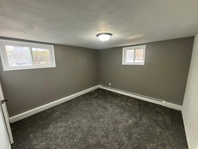 basement with a baseboard radiator, plenty of natural light, and dark colored carpet