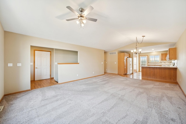 unfurnished living room featuring lofted ceiling, ceiling fan with notable chandelier, and light carpet