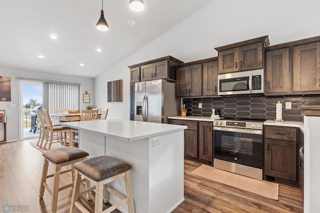 kitchen featuring hardwood / wood-style floors, lofted ceiling, a kitchen island, and appliances with stainless steel finishes