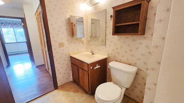 half bathroom featuring wallpapered walls, baseboard heating, vanity, and toilet