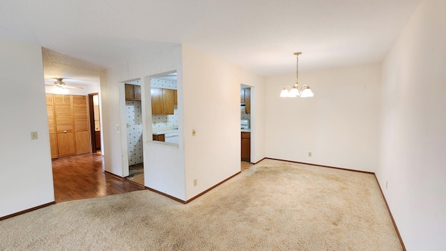 spare room featuring baseboards, light carpet, and ceiling fan with notable chandelier