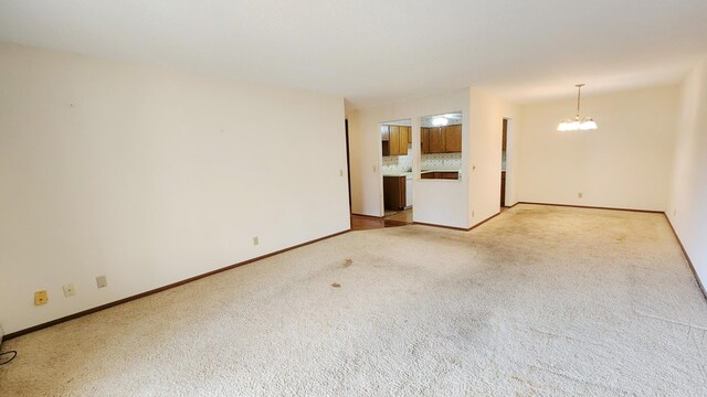 unfurnished living room featuring light colored carpet, an inviting chandelier, and baseboards