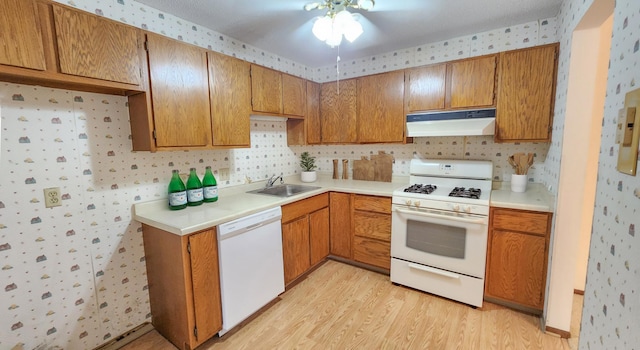 kitchen featuring under cabinet range hood, light countertops, a sink, white appliances, and light wood-style flooring