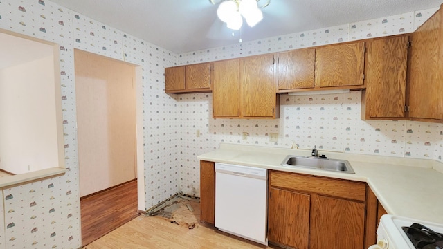 kitchen featuring stove, wallpapered walls, a sink, white dishwasher, and light wood-style flooring