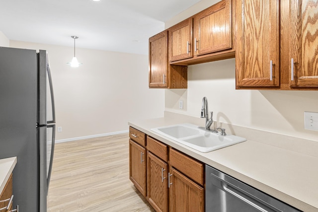 kitchen with stainless steel appliances, sink, pendant lighting, and light wood-type flooring